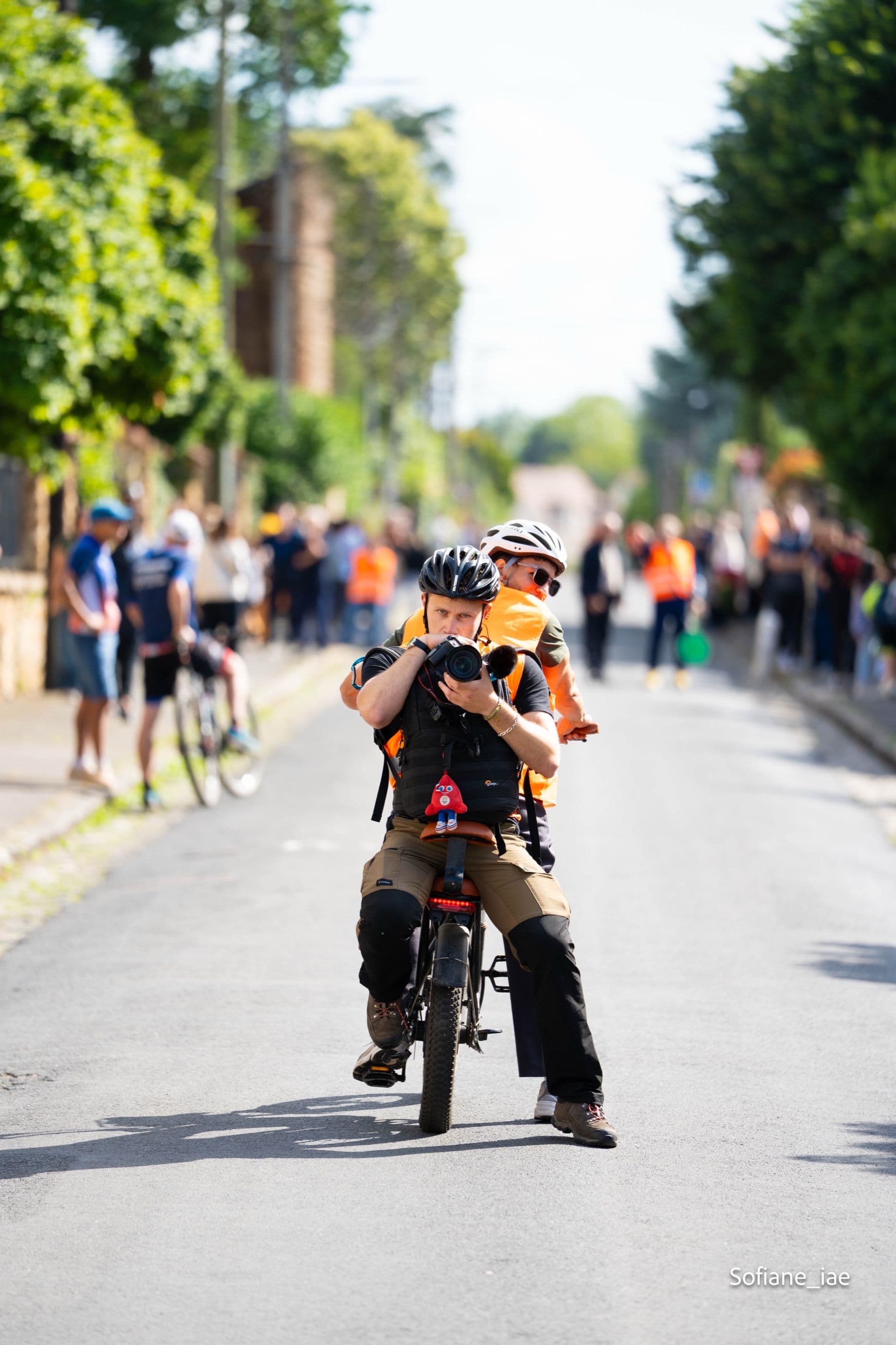 Le photographe en action, appareil au poing, depuis son vélo